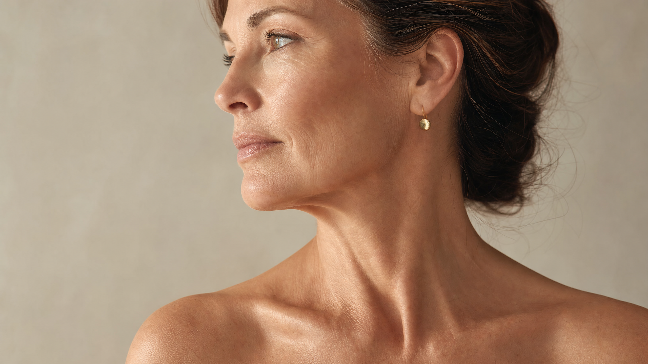Editorial portrait of a woman in her late 40s showing visible skin laxity at the jawline and neck — illustrating the visible signs of sagging skin and collagen loss